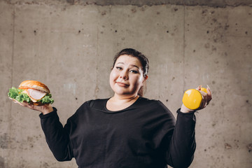 sport with unhealthy food. combination of active life with fast food. close up photo. fat woman...