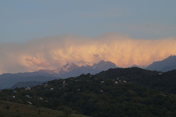 Beautiful rural landscape. Summer sunset in the mountains. A white cloud covers the tops of the mountains like a big ocean wave. Asia. Tien Shan.