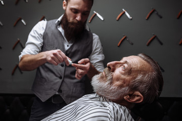 Caucasin old man getting his beard shaved by barber visiting hairtician at shaving saloon, close up