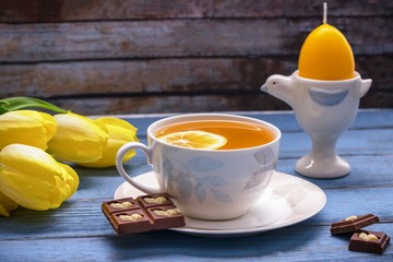 Happy Easter. Lemon tea, milk chocolate with easter bunny, yellow tulips, easter yellow candle in egg form on vintage background
