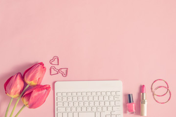 Blogger or freelancer workspace with keyboard and red tulips on pink background
