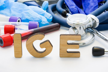 Medical abbreviation IGE in laboratory diagnostics. Letters, create words IGM, meaning Immunoglobulin E antibody, are surrounded by test tubes with blood, stethoscope and other medical equipment