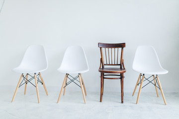 Modern style of three plastic chairs versus Vintage style of one brown wooden chair with background of white painted wall for loft decoration idea of house, office or shop