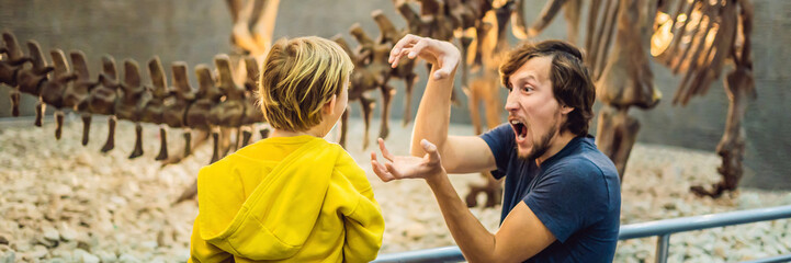 Dad and boy watching dinosaur skeleton in museum BANNER, LONG FORMAT