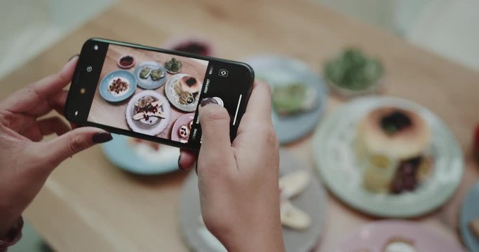A girl trying to perfect her angle while taking pictures of delicious looking food.