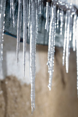 Icicles on an old, rusty, rural roof. Clay wall