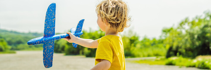 Happy kid playing with toy airplane against old runway background. Traveling with kids concept BANNER, LONG FORMAT