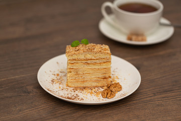 Piece of cake Napoleon on white plate on wooden background. Russian cuisine, layered cake with cream, close up view. Selective focus.