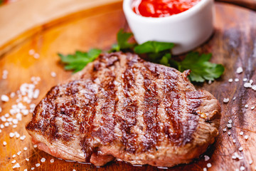 Grilled beef steak with tomato sauce on wooden cutting board. Close up