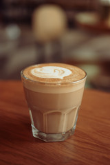 Cappuccino or flat-white coffee served in small glass on tabletop in cafe