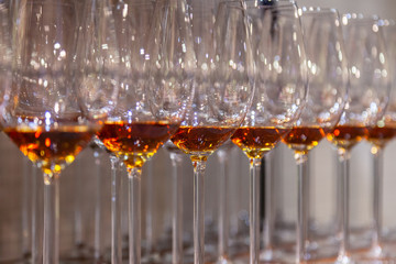 Many transparent crystal wine glasses with cognac stand in row on brown wooden shelves of  rack. Side view. The concept of tasting whiskey, brandy, port on the production in Scotland, Ireland, France