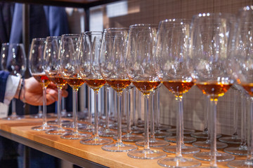 Professional man-cavist takes wine glass with cognac from wooden shelf in liquor store. Concept of degustation spirits: whiskey, brandy, rum, sherry, porto, bitter on bartenders competition