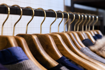 Many wooden hangers with different male clothes in boutique on metal stand. Closeup, side view. Concept opening of luxury business fashion store for managers