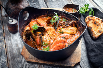 Traditional Catalan fish stew romesco de peix with prawns, mussels and fish as closeup in a modern...
