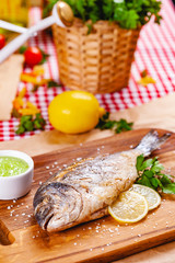 Grilled dorado fish with lemon and sauce on wooden board. Close up