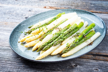 Traditionell gekochter deutscher weißer und grüner Spargel mit Buttersauce dekoriert mit Kresse als closeup auf einem Modern Design Teller auf einem Holztisch 