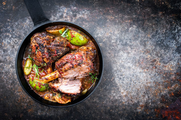 Traditional barbecue leg of lamb with lemon and tomatoes as top view in a cast-iron skillet with copy space right