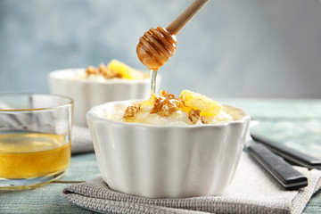 Pouring honey onto rice pudding with walnuts and orange slice in ramekin on table