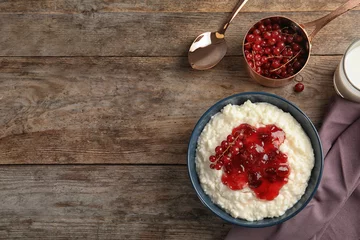 Raamstickers Creamy rice pudding with red currant and jam in bowl served on wooden table, top view. Space for text © New Africa