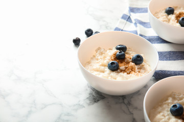 Creamy rice pudding with cinnamon and blueberries in bowls on marble table. Space for text