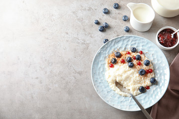 Creamy rice pudding with red currant and blueberries in bowl served on grey table, top view. Space for text