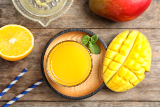 Glass of fresh mango drink and tropical fruits on wooden table, top view