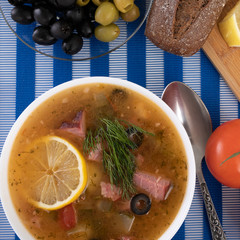 Traditional Russian soup Solyanka cooked with meat, sausages, salted cucumbers on wite bowl. Black...