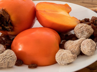 Delicious fresh persimmon fruit , raisins and dried figs  on the plate  and wooden table