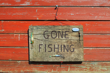 gone fishing sign written on a wooden plaque hanging on a fence