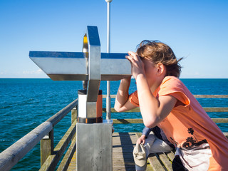 Boy is looking through a binocular at the sea