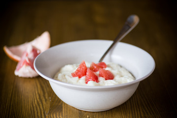 sweet boiled semolina porridge in a plate with slices of red grapefruit