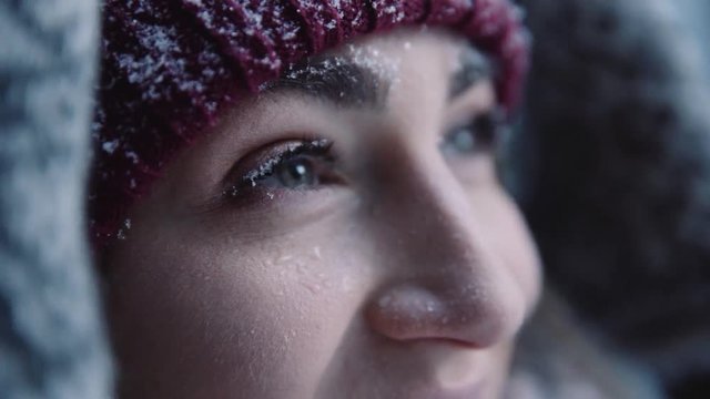 Young woman with beautiful eyes in hat snow falls on face smiling in winter park cold girl happy nature white holiday outdoor pretty attractive fashion fun happiness model portrait slow motion