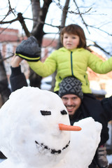 Dad and son make a big snowman . Happy family play on snow in backyard