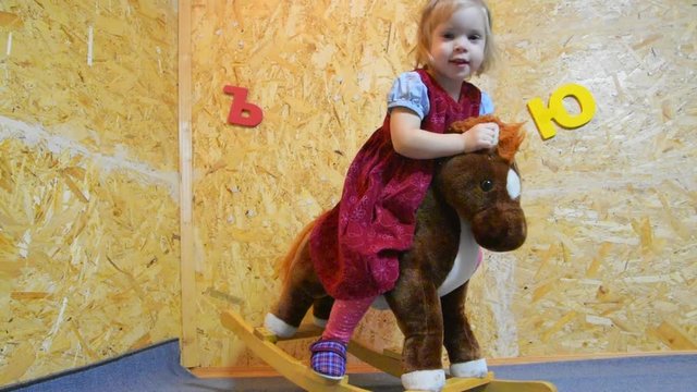 the girl, child on a horse toy, ride, swing in the nursery