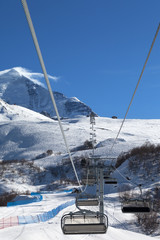 Chair-lift and ski slope in snowy mountains at sunny winter day