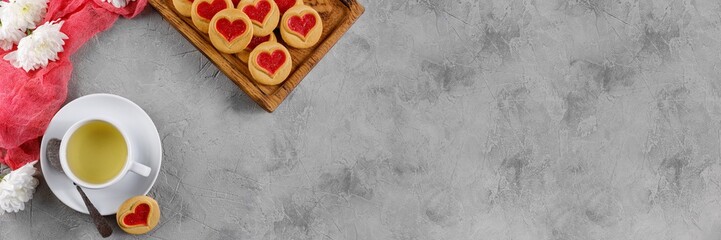 Cup with green tea and cookies with a heart on a decorative board is an ornament from fresh flowers. Valentine's day concept. Banner.