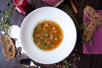 vegetable soup in a round white plate on a dark wooden table next to the bread candle and table decorations
