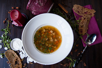 vegetable soup in a round white plate on a dark wooden table next to the bread candle and table decorations