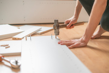 close up man assembling brand new furniture with the hammer on the wooden floor n