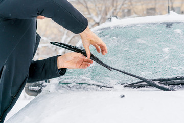 man adjusting and cleaning wipers of car in snowy weather b