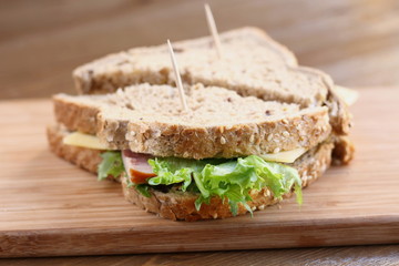 Delicious sandwich with natural green salad lettuce, cheese and ham, whole grain bread on a wooden plate board as a healthy snack for lunch