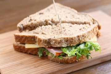 Delicious sandwich with natural green salad lettuce, cheese and ham, whole grain bread on a wooden plate board as a healthy snack for lunch