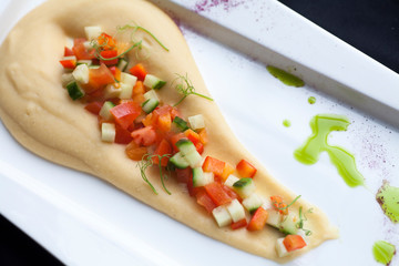 hummus with chopped vegetables on top on a white plate stands on a black background