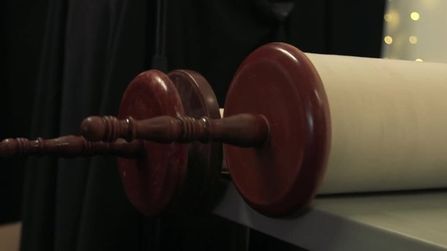 The end rollers of a large ceremonial torah scroll roll to the edge of a table