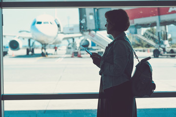 Young woman in the airport, looking through the window at planes