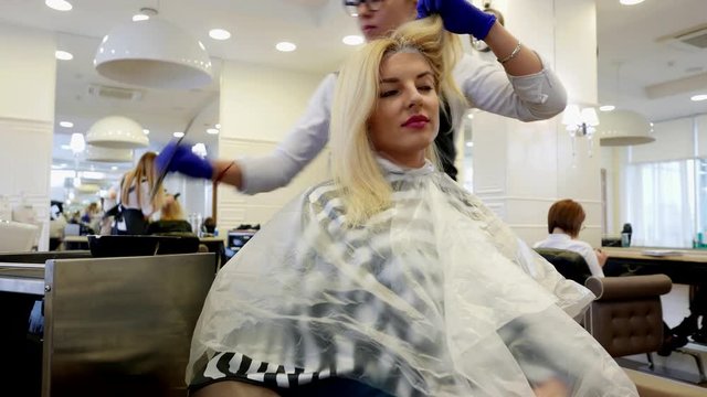 Hairdresser dyes the hair of an attractive blonde girl in a beauty salon.