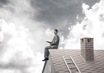 Student guy in suit on brick house roof reading book