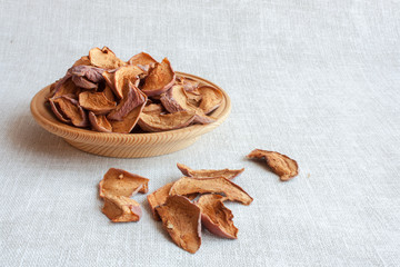 dried apples on a wooden plate on a grey linen background