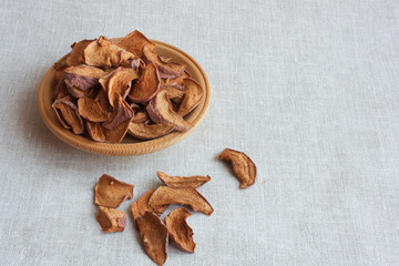 dried apples on a wooden plate on a grey linen background