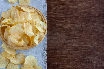 potato chips on wooden plate on linen napkin on brown wooden background